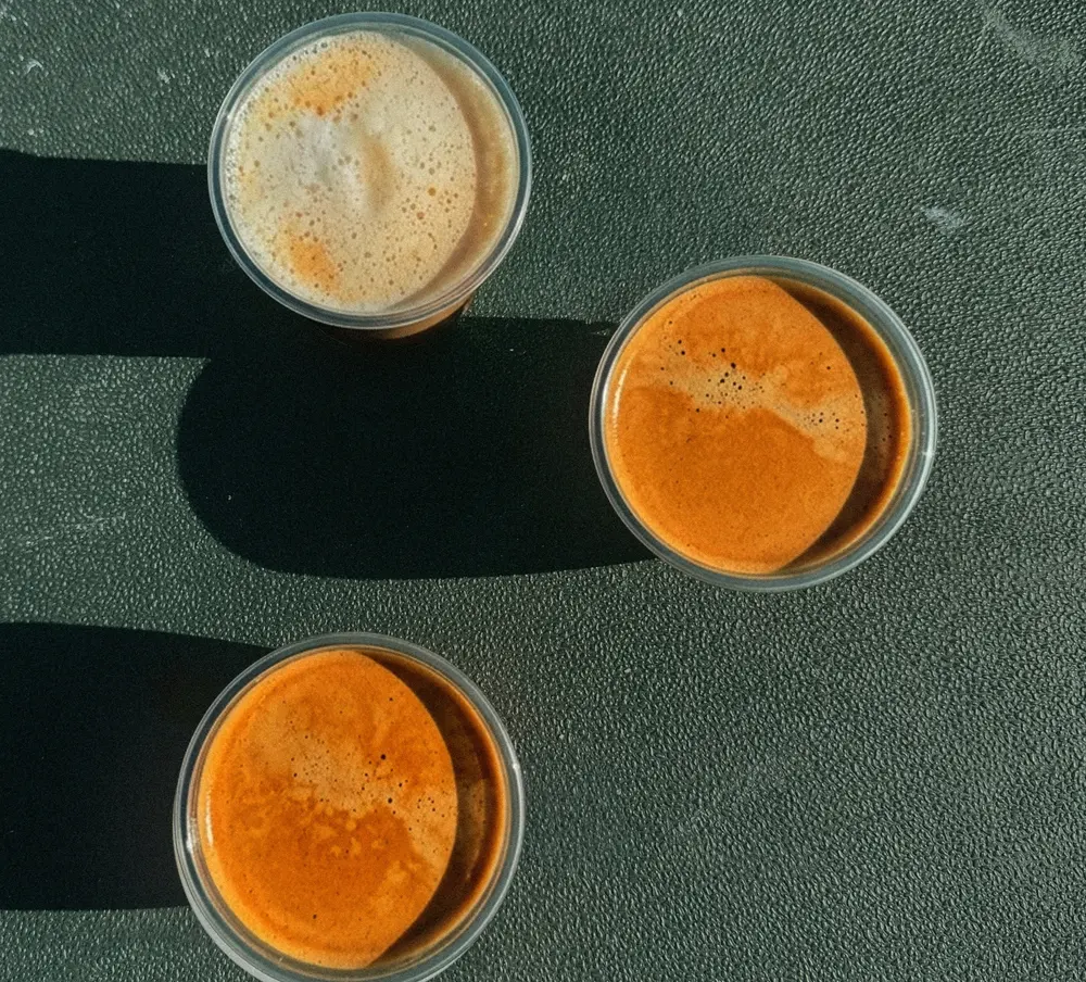 Tres cafés con crema vistos desde arriba, sobre fondo verde