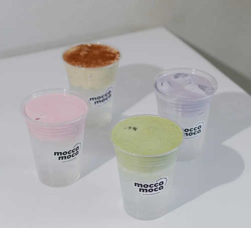 Cuatro bebidas frías de colores en los vasos de mocca moca, sobre una mesa blanca