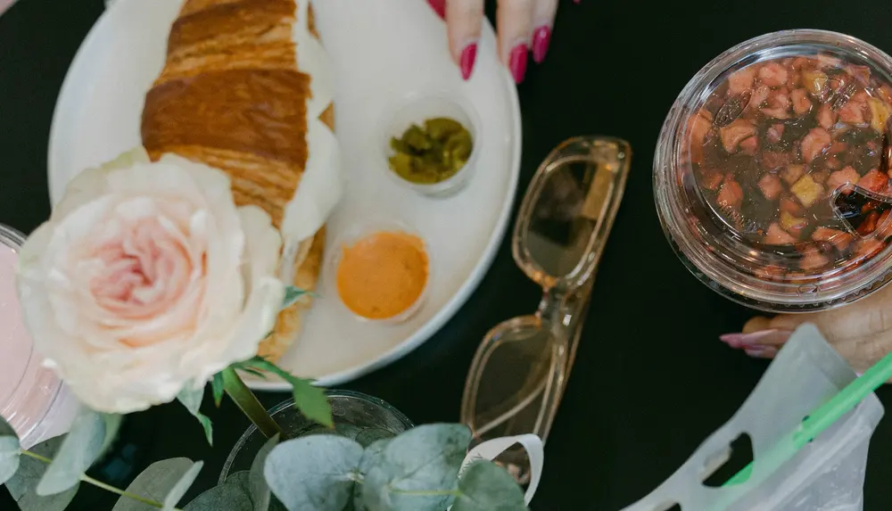 Mesa vista desde arriba con croissant, una rosa, pretzels y un matcha